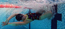 Person swimming underwater in a pool with colorful swim shorts and a swim cap.