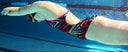 Person swimming underwater in a pool with colorful swim cap and goggles.